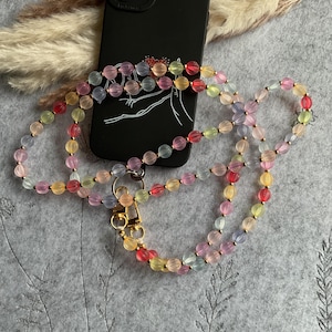Peut inclure: Une dragonne de téléphone en perles colorées avec un fermoir doré. Les perles sont translucides et se déclinent dans des tons de rose, rouge, jaune et bleu.