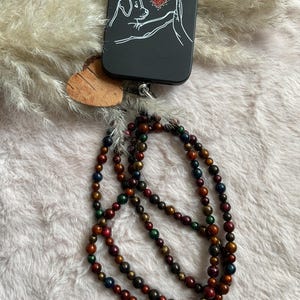 Op de afbeelding: Zwarte telefoonhoes met een honden- en handontwerp, een houten hartvormige bedel en een kralenketting met rode, groene en blauwe kralen. De telefoonhoes heeft een rood hartdetail.