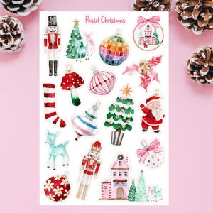 May include: A sheet of pastel Christmas stickers featuring festive designs. The stickers include a nutcracker, Christmas trees, baubles, Santa Claus, a mushroom, a deer, and a house. The text "Pastel Christmas" is at the top. The stickers are in pink, green, red, and gold.