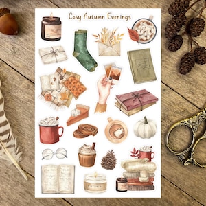 May include: A sheet of stickers with a watercolor illustration theme of cozy autumn evenings. The stickers feature images of books, candles, mugs of hot drinks, fall leaves, and other autumnal elements. The text "Cosy Autumn Evenings" is at the top of the sheet.