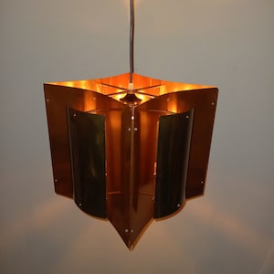 May include: A copper and brass pendant light fixture with a geometric design. The light is on and illuminating the room.