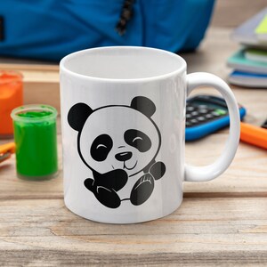 Pu&ograve; includere: Tazza in ceramica bianca con un design di panda cartoon in bianco e nero. Il panda sorride e tiene le zampe insieme.
