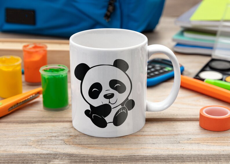 Pu&ograve; includere: Tazza in ceramica bianca con un design di panda cartoon in bianco e nero. Il panda sorride e tiene le zampe insieme.