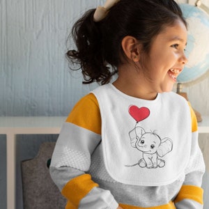 May include: A white bib featuring a black and white illustration of an elephant holding a red heart-shaped balloon. The bib is being worn by a young child with dark hair.