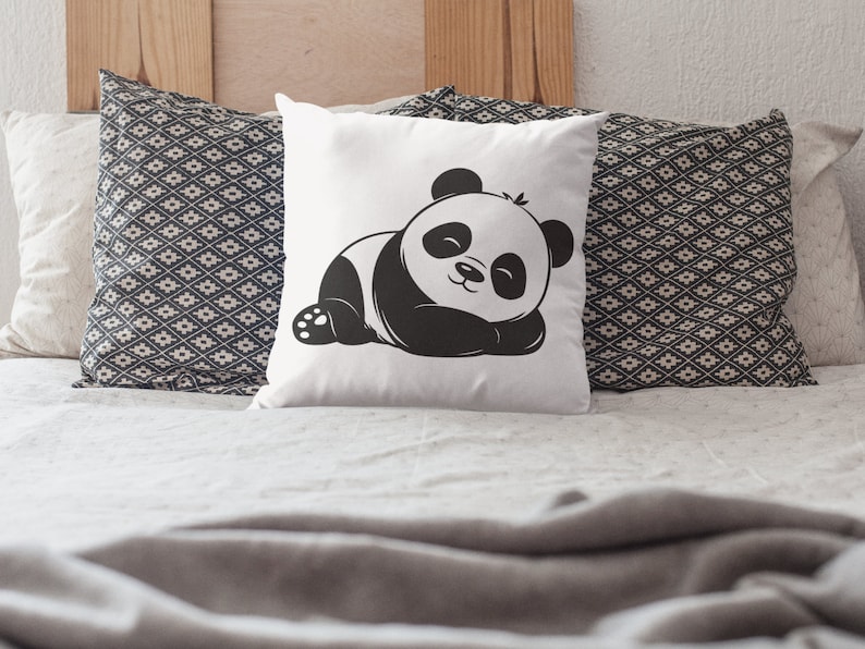 Pu&ograve; includere: Un cuscino bianco con un'illustrazione di un orso panda bianco e nero. Il panda &egrave; sdraiato con gli occhi chiusi. Il cuscino &egrave; su un letto con una coperta grigia.