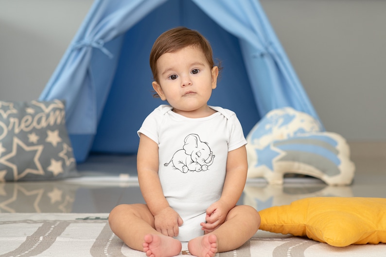 May include: A baby wearing a white onesie with a black and white illustration of a sleeping elephant. The baby is sitting on a gray and white patterned rug in front of a blue play tent.