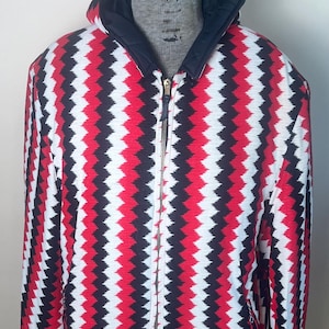 May include: A red, black, and white patterned hooded jacket with a zipper closure. The jacket has a chevron pattern.