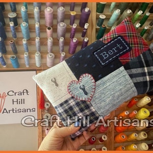 May include: A patchwork fabric pouch with a heart and a small crab design. The pouch has a red and black tartan fabric on one side and a blue fabric with white polka dots on the other side. The pouch is personalised with the name "Bert" in a black rectangle. The pouch is held in a hand against a background of spools of thread.