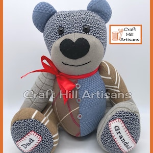 May include: A grey and blue patchwork teddy bear with a red ribbon, buttons, and embroidered details. The bear's paws have the words "Dad" and "Granddad" embroidered on them. The bear is sitting on a white background. Craft Hill Artisans is printed on a label in the top right corner.