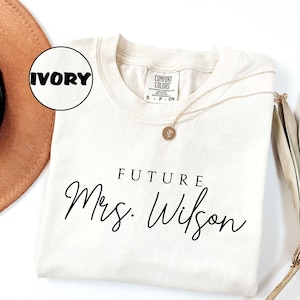 May include: Ivory t-shirt with the text "FUTURE Mrs. Wilson" in black script font.