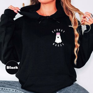 Pode incluir: Camisola de moletom com capuz preta com o texto "Spooky Nurse" e um fantasma de desenho animado usando um chap&eacute;u de enfermeira.
