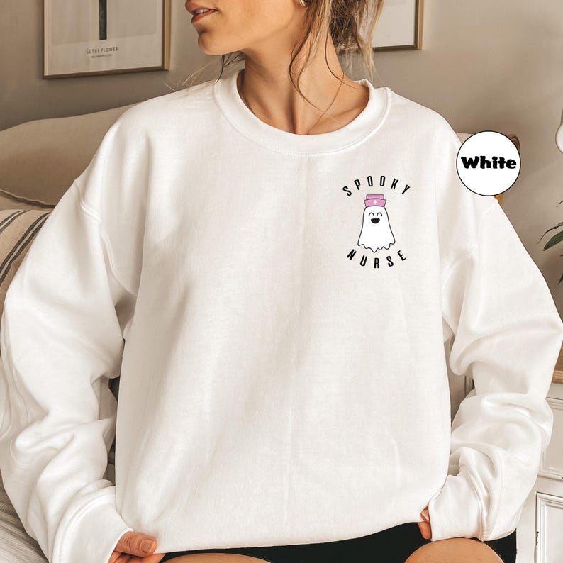 Pode incluir: Camisola branca com um gr&aacute;fico de um fantasma usando um chap&eacute;u de enfermeira e o texto "Spooky Nurse".