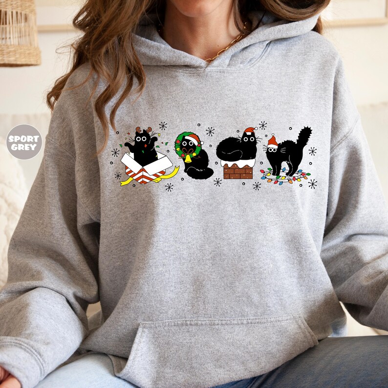 May include: A gray hoodie with a black cat Christmas design. The cats are wearing Santa hats, a reindeer antler headband, and a Christmas wreath. The design includes a chimney, a gift box, and Christmas lights.