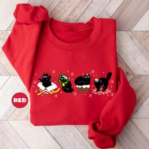May include: Red Christmas sweatshirt with a black cat design. The cats are wearing Santa hats and are in various festive poses. The text on the sweatshirt says "Merry Catmas".