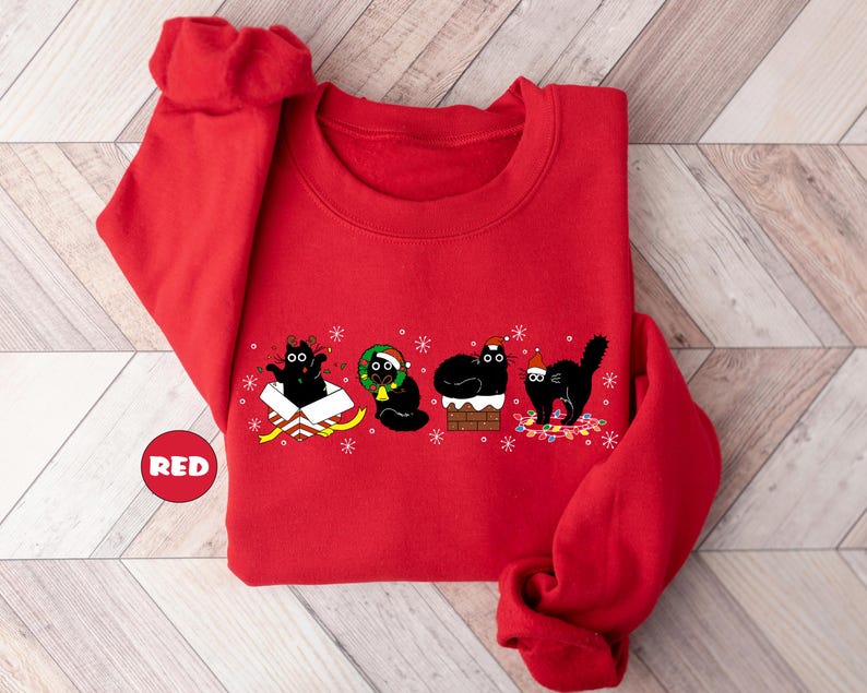 May include: Red Christmas sweatshirt with a black cat design. The cats are wearing Santa hats and are in various festive poses. The text on the sweatshirt says "Merry Catmas".