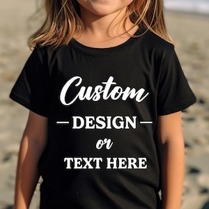Puede incluir: Camiseta negra con texto blanco "Custom - DESIGN - or TEXT HERE". La camiseta de cuello redondo est&aacute; hecha de un material suave. El dise&ntilde;o es para ni&ntilde;os.