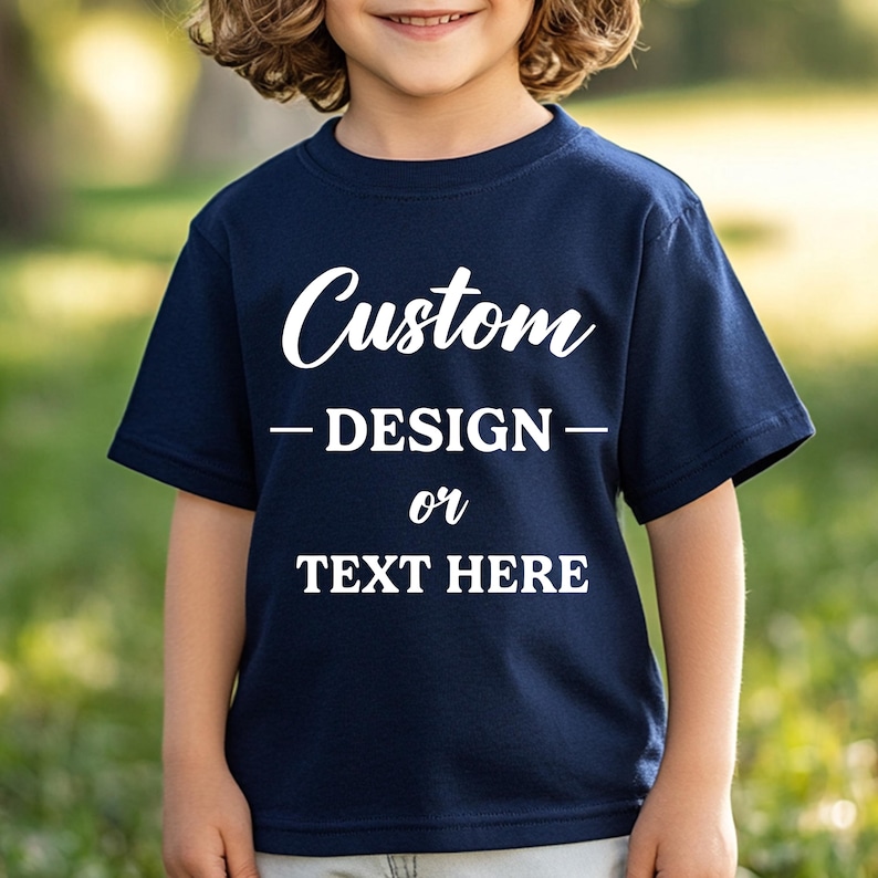 Puede incluir: Camiseta azul marino con las palabras "Custom DESIGN or TEXT HERE" en blanco. La camiseta de manga corta parece estar hecha de un material suave. El fondo borroso sugiere un entorno al aire libre.