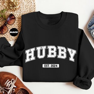 May include: Black sweatshirt with white text that reads "Hubby Est. 2024".