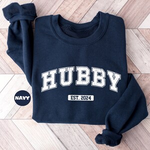 May include: Navy blue sweatshirt with white text that reads "HUBBY EST. 2024".
