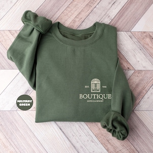May include: A military green sweatshirt with a white logo that says "Boutique Hotel & Resort" with the text "EST. 1993" above the logo.
