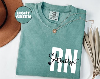 May include: A light green t-shirt with a white graphic of a stethoscope and the letters RN with the name Emily written in cursive underneath.