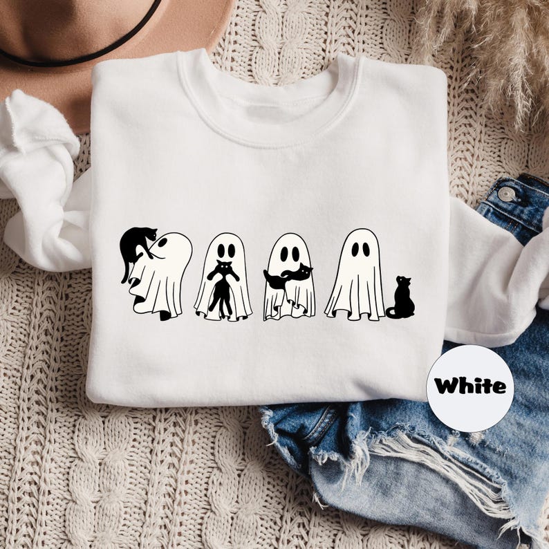 Pode incluir: Camisola branca com um gr&aacute;fico de quatro fantasmas segurando gatos pretos. O texto "White" &eacute; vis&iacute;vel numa etiqueta branca.