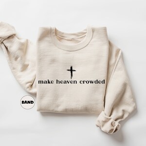 May include: A beige sweatshirt with a black cross and the text "make heaven crowded" printed on the front.