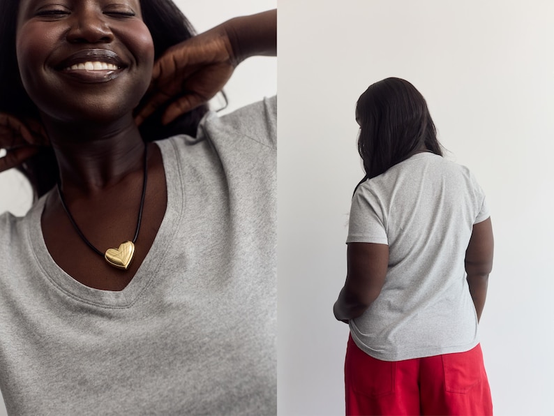K&ouml;nnte beinhalten: Ein graues kurz&auml;rmeliges T-Shirt mit V-Ausschnitt, kombiniert mit einem goldenen herzf&ouml;rmigen Anh&auml;nger an einer schwarzen Kordelkette. Das T-Shirt ist von vorne und hinten zu sehen, wobei die R&uuml;ckansicht einen schlichten grauen Stoff zeigt.