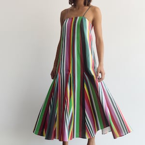 May include: A sleeveless midi dress featuring a vibrant vertical striped pattern in shades of green, red, yellow, purple, black, and white. The garment has a straight neckline, thin spaghetti straps, and a flared skirt with pleats at the hem.