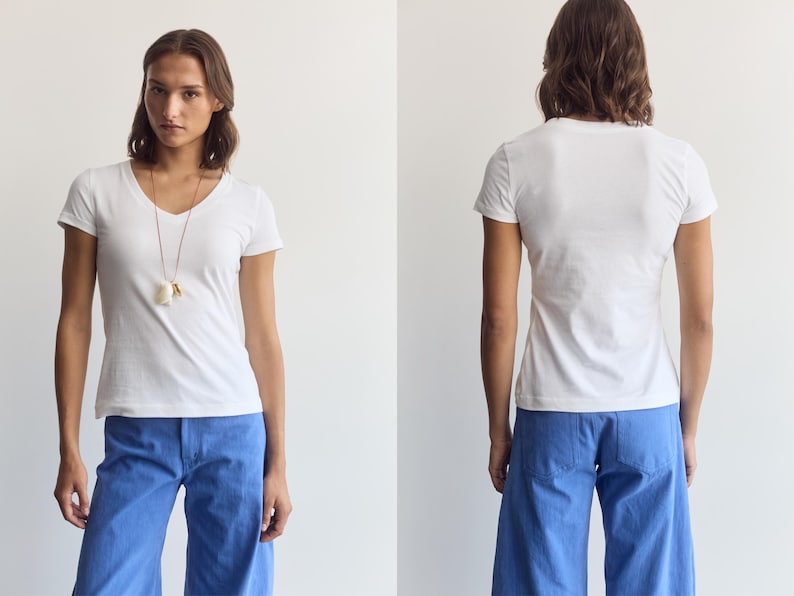 K&ouml;nnte beinhalten: Ein schlichtes wei&szlig;es kurz&auml;rmeliges T-Shirt mit V-Ausschnitt kombiniert mit einer leuchtend blauen weiten Hose. Das T-Shirt hat eine einfache, k&ouml;rpernahe Passform, w&auml;hrend die Hose einen geraden Schnitt mit sichtbaren Ges&auml;&szlig;taschen aufweist.
