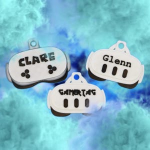 May include: Three white and black gamer tags with the names "Clare" and "Glenn" and the word "GAMERTAG" printed on them. The tags have a controller design with black buttons and are set against a blue and white background.