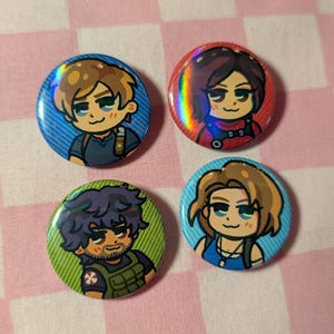 May include: Four circular pin-back buttons featuring chibi-style character illustrations. One button has a blue background with a brown-haired character, one is red with a dark-haired character, one is green with a bearded character, and one is blue with a light-brown-haired character.