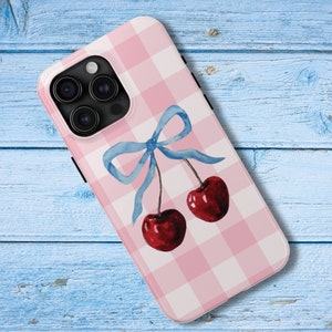 May include: A pink and white gingham phone case with a blue bow and two red cherries.