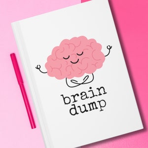 Könnte beinhalten: Ein weißes Notizbuch mit einer rosa Gehirn-Karikatur, die meditiert, mit dem Text "brain dump" darauf. Ein rosa Stift liegt auf einer rosa Oberfläche neben dem Notizbuch.