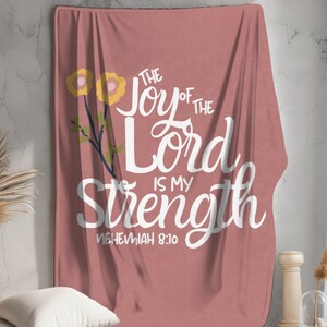 May include: A pink throw blanket with a white floral design and the text "The Joy of the Lord is My Strength Nehemiah 8:10".