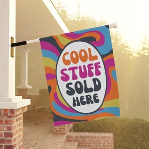 May include: A colorful outdoor flag with the text "COOL STUFF SOLD HERE" in a retro font. The flag features a vibrant design with orange, pink, blue, and yellow wavy patterns, perfect for a shop or business.