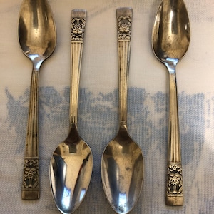 Puede incluir: Cuatro cucharas de plata con diseños florales ornamentados en los mangos. Las cucharas tienen un estilo clásico y vintage.