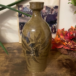 May include: A handcrafted, brown ceramic vase with a unique, textured design. The vase features a wide base that tapers upwards, with a flared rim. Dark brown leaf-like patterns adorn the surface. The vase is approximately 25 cm tall.