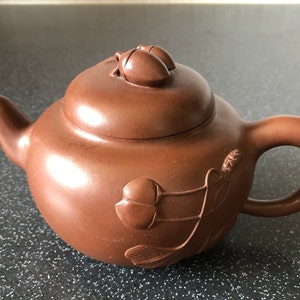 Puede incluir: Tetera de cerámica marrón con tapa y asa curva. La tetera está decorada con diseños florales y tiene un pico para verter. La tetera es de estilo tradicional y probablemente se utiliza para preparar té.