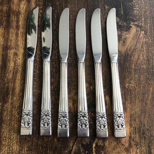 Könnte beinhalten: Sechs silberne Essmesser mit verzierten Blumendesigns auf den Griffen.