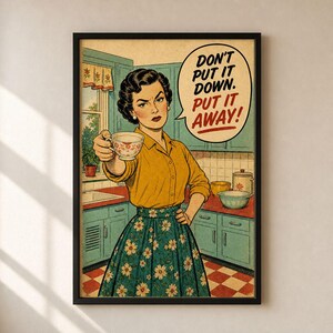 May include: A framed wall art print featuring a person in a yellow shirt and floral skirt holding a teacup in a kitchen. A speech bubble contains the text: DON'T PUT IT DOWN. PUT IT AWAY! The scene includes teal cabinets, a checkered floor, and a window.