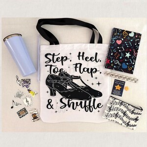 May include: A white tote bag with black handles featuring a graphic of tap shoes and the text Step, Heel, Toe, Flap, & Shuffle. Included are a light blue tumbler, a spiral notebook with musical notes, a small zipper pouch, and various stickers.