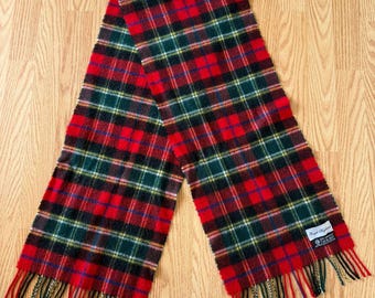 May include: A red, green, and black plaid scarf with fringed ends. The scarf features a classic tartan pattern with a label on one end. The scarf is made of a soft material and is suitable for cold weather.