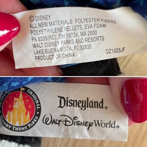 Puede incluir: Una etiqueta blanca con texto negro que dice "Disney. Todos los materiales nuevos: fibras de poli&eacute;ster, gr&aacute;nulos de polietileno, espuma EVA. PA 8335(RC), OH 18724, MA 2000. Walt Disney Parks and Resorts. Lake Buena Vista, FL 32830. Producto de China. DZ1023JF". Debajo de la etiqueta hay una etiqueta blanca con texto negro que dice "Disneyland. Walt Disney World&reg;" y un logotipo de castillo rojo y blanco con el texto "Authentic Original Disney Theme Parks".