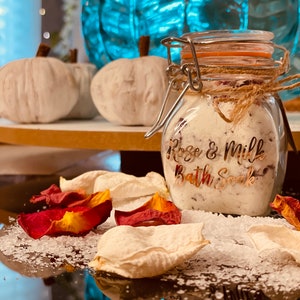 May include: A glass jar filled with white bath soak and rose petals. The jar has a gold label that reads "Rose & Milk Bath Soak".