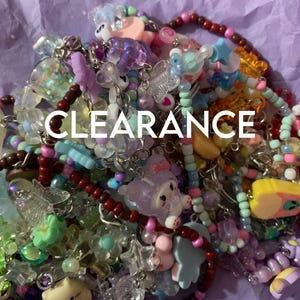 May include: A collection of colourful beaded bracelets and charms featuring various shapes including flowers, stars, butterflies, and a cartoon character, with the word CLEARANCE overlaid in white text across the centre of the image.