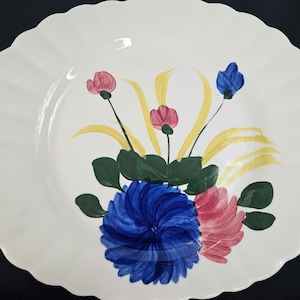 May include: A white ceramic oval platter with a scalloped edge features a hand-painted floral design. The design includes blue, pink, yellow, and green flowers and leaves.