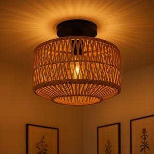 May include: A woven rattan ceiling light fixture. The light has a cylindrical shade with a crisscross pattern and a black base. The light bulb is visible inside the shade, emitting a warm glow. The fixture is mounted on a white ceiling.