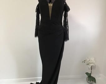 Puede incluir: Un vestido negro de hombros descubiertos con mangas largas de encaje y un escote de corazón. El vestido tiene un corpiño ajustado y una falda fluida.
