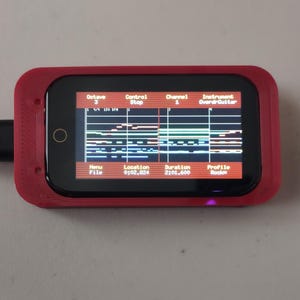 Könnte beinhalten: Ein rechteckiges rotes elektronisches Gerät mit einem schwarzen Bildschirm, der Daten wie Octave, Control, Channel, Instrument, Menu, Location, Duration und Profile anzeigt. Ein schwarzes USB-Kabel verbindet das Gerät mit einem silbernen Laptop-Anschluss.